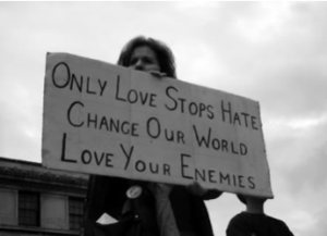 Woman holding protest sign which reads "love your enemies."