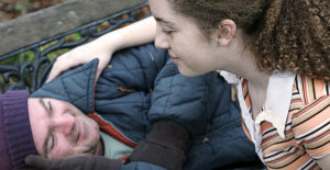 woman helping homeless man on park bench
