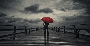 Person standing on dock with red umbrella watching on coming storm