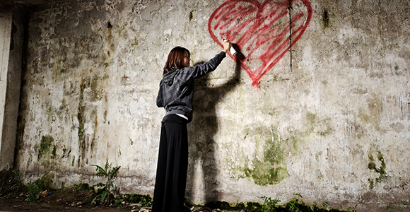 girl spray painting a graffiti heart on wall
